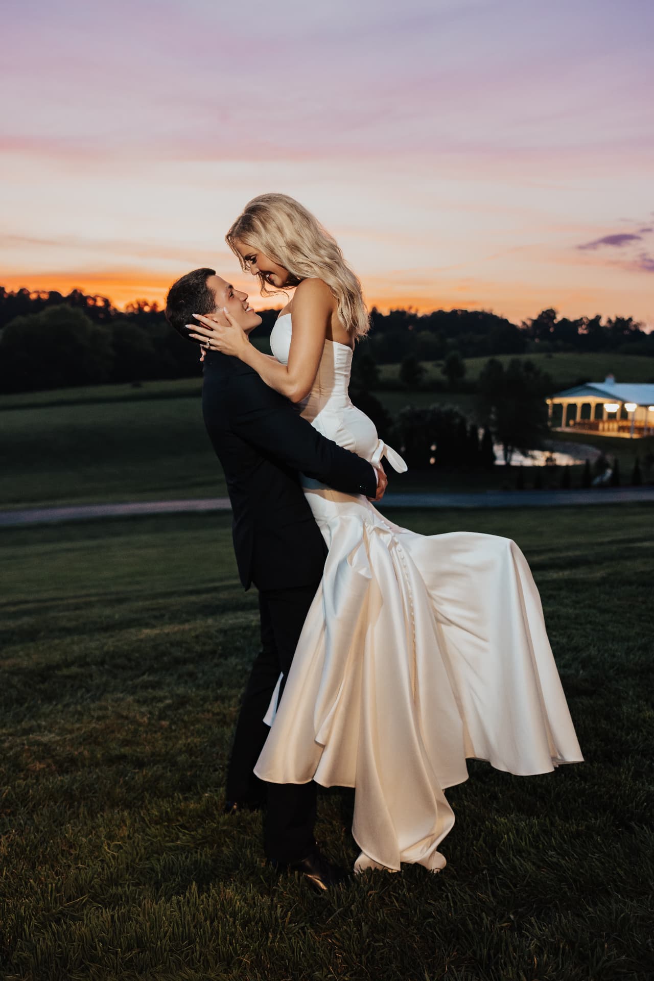 Groom lifting bride against a dramatic sunset sky